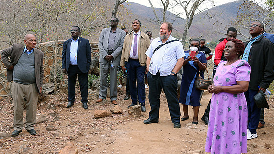 Greater Nhiwatiwa (im violetten Kleid), Ehefrau von Bischof Eben K. Nhiwatiwa (links), erklärt der Gruppe afrikanischer EmK-Bischöfe die Geschichte und Bedeutung einer für Simbabwe historischen methodistischen Gebetsstätte.