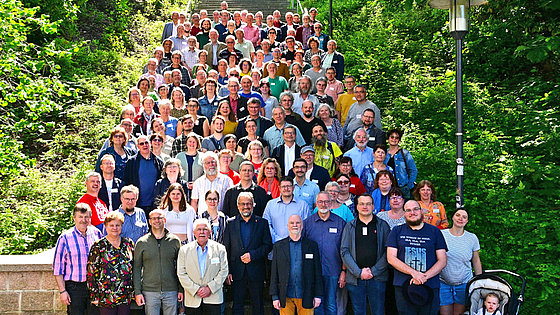 Gruppenbild der Pastoren und Pastorinnen der Ostdeutschen Jährlichen Konferenz sowie den gewählten Delegierten. Sie stehen auf einer hohen Steintreppe, die von Bäumen und Sträuchern umgeben ist.