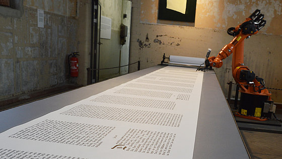 Ein Roboter der Firma Kuka, der bei der Weltausstellung Reformation 2017 in Wittenberg fortlaufend den Text der Bibel auf eine endlos erscheinende Papierrolle auftrug.