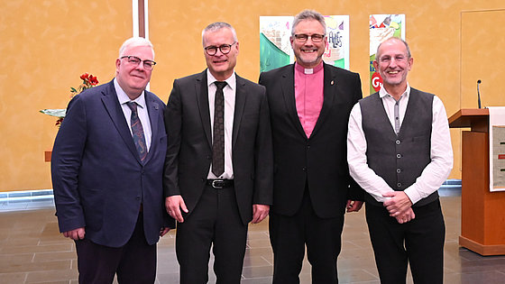 Vier Männer stehen nebeneinander in einem Kirchensaal vor Abendmahlstisch und Banner. Von links nach rechts: Simon Jost, Michael Löffler, Bischof Werner Philipp und Klaus Ulrich Rouf. Alle tragen formelle Kleidung und blicken freundlich in die Kamera.