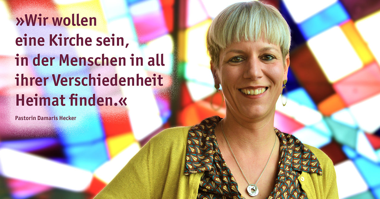 Vor einem Buntglasfenster steht eine fröhlich lächelnde Frau mit heller Kurzhaarfrisur. Sie trägt eine bunte Bluse und senfgelbe Strickjacke. Es ist Pastorin Damaris Hecker, die EmK-Beauftragte für Menschen verschiedener Lebens- und Liebensweisen.