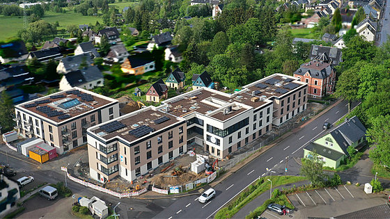 Ein Luftbild zeigt schräg von oben die aus drei Gebäuden bestehende diakonische Einrichtung Bethanien-Campus. Moderne, dreistöckige Bauten mit Balkonen und Solaranlage auf dem Dach. Umgeben von Häusern des erzgebirgischen Ortes Scheibenberg.