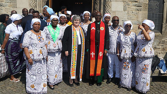 Vor einem Kircheneingang stehen etwa zwei Dutzend Menschen, mehrheitlich Frauen. Einige von ihnen schauen in die Kamera. Viele von ihnen sind einheitlich gekleidet. Auf ihrer Kleidung steht der Name ihrer heimatlichen Kirche: Methodist Church Ghana.