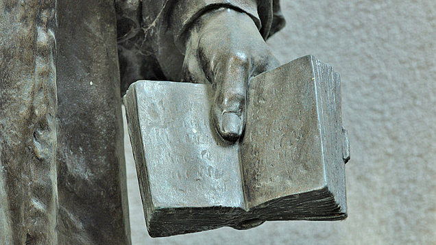 Ausschnitt einer Wesley-Skulptur, die mit der linken Hand gehalten eine geöffnete Bibel  zeigt.