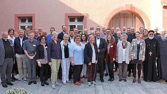 Vor einem Haus steht eine Gruppe von 39 Personen, darunter 12 Frauen. Manche Männer tragen Kleidung, durch die sie als Geistliche erkennbar sind. Harald Rückert, der Bischof der EmK für Deutschland, steht etwa in der Mitte.