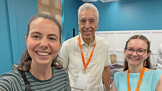 Lea Schmidt (links, gestreiftes Shirt), Bischof Ruben Saenz Jr. (Mitte, weißes Hemd) und Imke Sewing (rechts, hellblaues Oberteil) stehen bei der Global Young People’s Convocation in Dublin zusammen. Alle drei lächeln in die Kamera.