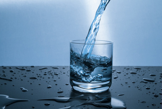 Ein Glas, das mit Wasser gefüllt wird als Sinnbild für den Durst des Menschen.