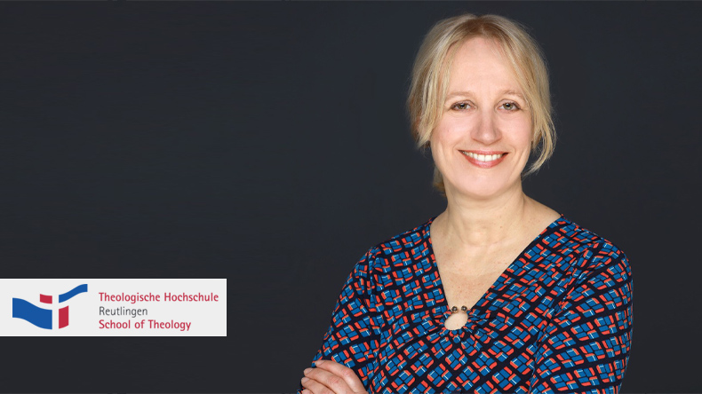 Im Bild blickt die neu gewählte Professorin der Theologischen Hochschule Reutlingen den Betrachter mit einem Lächeln an. Kathrin Liess hat halblange, blonde, mittelgescheitelte Haare und trägt ein blau-rot-schwarz-kariertes Kleid.