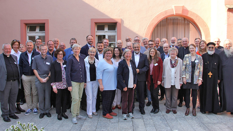 Vor einem Haus steht eine Gruppe von 39 Personen, darunter 12 Frauen. Manche Männer tragen Kleidung, durch die sie als Geistliche erkennbar sind. Harald Rückert, der Bischof der EmK für Deutschland, steht etwa in der Mitte.