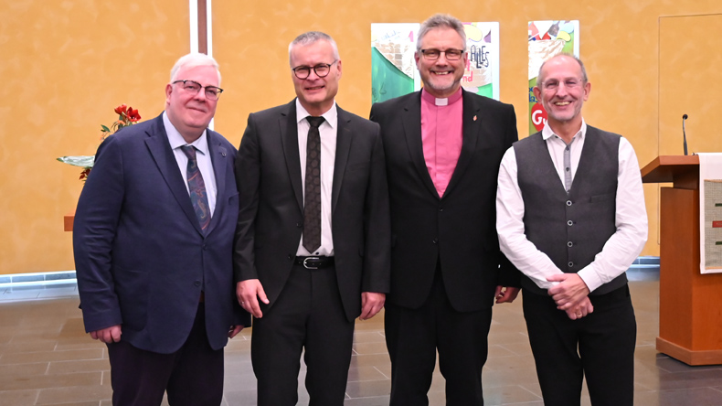 Vier Männer stehen nebeneinander in einem Kirchensaal vor Abendmahlstisch und Banner. Von links nach rechts: Simon Jost, Michael Löffler, Bischof Werner Philipp und Klaus Ulrich Rouf. Alle tragen formelle Kleidung und blicken freundlich in die Kamera.