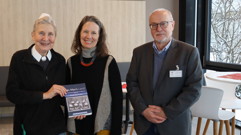 Schwester Roswitha Müller, Priscilla Pope-Levison und Ludwig Wolf stehen in einem hellen Raum. Schwester Roswitha hält das Buch »No Man’s Land« in den Händen.