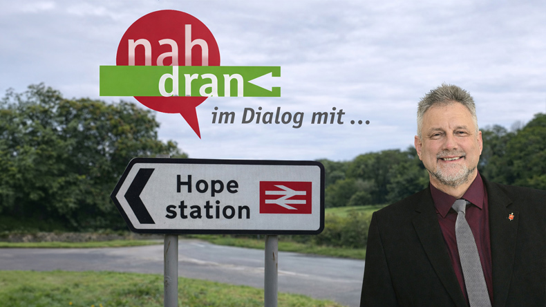 Fotomontage: Im Vordergrund sieht Bischof Philipp freundlich lächelnd in die Kamera. Daneben oben der grafisch aufbereitete Schriftzug »nah dran im Dialog mit …«. Darunter ein Wegweiser in Englisch: »Hope station«, zu Deutsch »Hoffnung Bahnhof«.